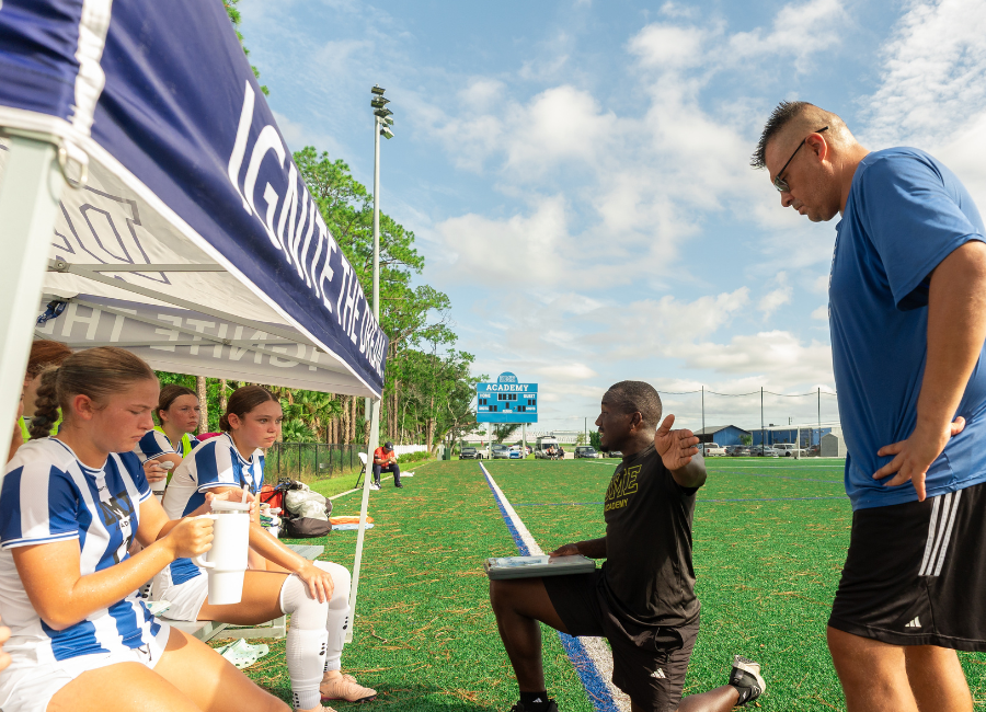 DME Academy girls soccer coaches give instructions to players on the sideline during a match in Daytona Beach, FL