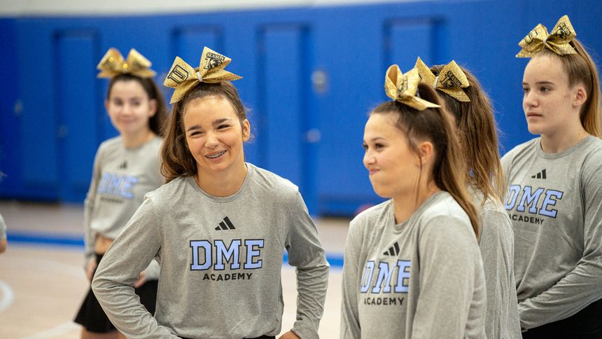Two DME cheer athletes in academy warm-ups between sessions.