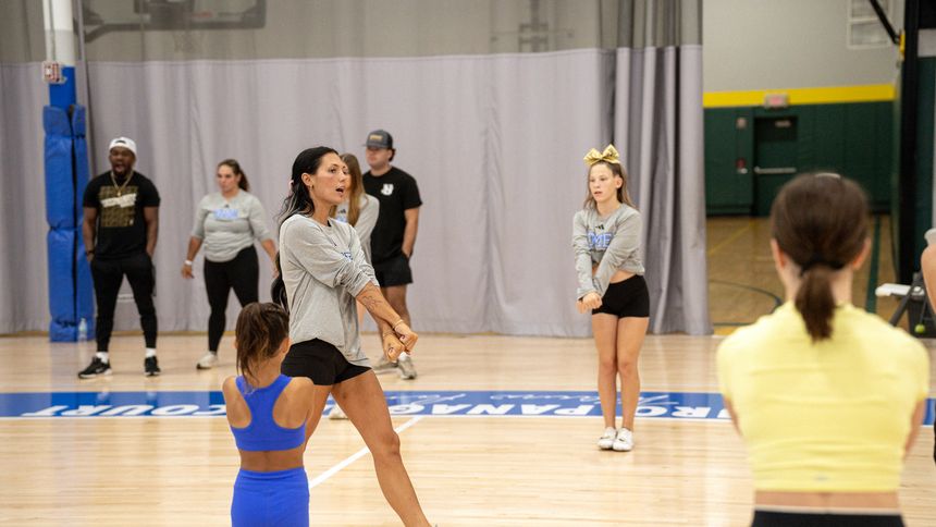 A large mixed-skill group of cheer athletes working with coaches on the DME floor.