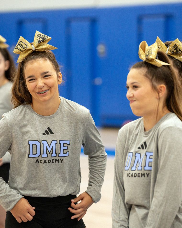 Two DME cheer athletes between sessions in academy warm-ups.